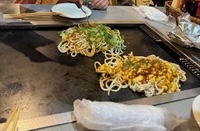 two noodle based hiroshima-style okonomyaki on a hot plate embedded in the restaurant table
