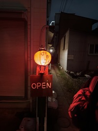 dark alley at night, illuminated by an orange lantern above an open sign