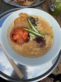 top view of a bowl of ramen with half a grilled potato and green okra shoots, broth is opaque