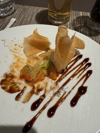 side view of fancy dinner plate, fried rice skin scupltured atop grilled veggies and sauce arranged in a ziczac fashion
