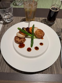 round slices of grilled vegies arranged in a semi circle crossed with green asparagus and brown sauce drops completing the circle