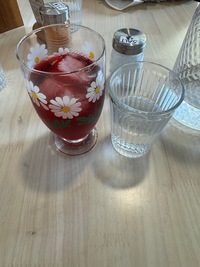 two drink glasses on a restaurant table, one filled with water and one with dark red hibiscus lemonade