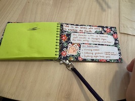 spiral notebook on table, left page is green, right page tells a story about the restaurant mascot Rin: she is an alien who came ot explore the earth. This character is Rin a Taiwanese staff mamber at marogoto vegan. Rin loves eating — especially unch plate! Her hobbies are: filming videos, collecting goshuin (temple and shrine stamps), exploring vegan foods spots