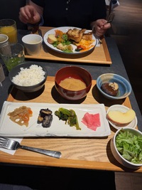 two breakfast trays, one with vegan french toast, one with various japanese veggies, salad, miso soup, rice and fruit, surrounded by various drinks