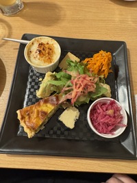 appetizer platter with quiche, carrot salad, vegan cheese slices, green lead salad, tiny mac and cheese bowl and pickeld cabbage salad